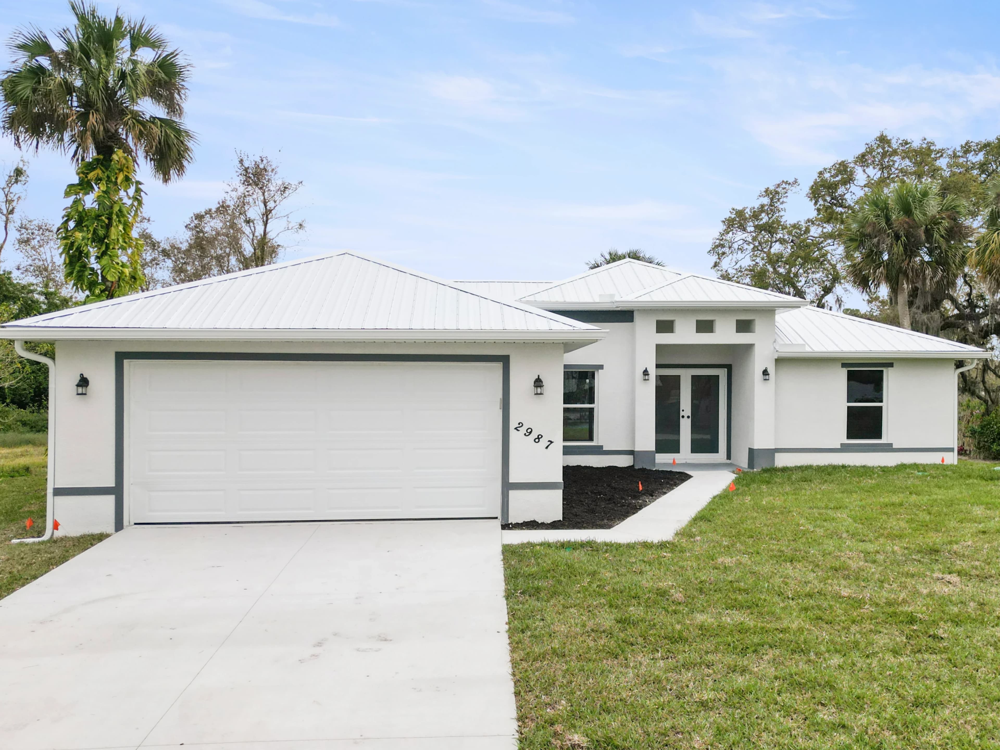 A newly constructed modern home in Florida featuring a durable white metal roof installed by Vreeland Roofing. Surrounded by lush greenery and palm trees, this home showcases expert roofing and construction craftsmanship.
