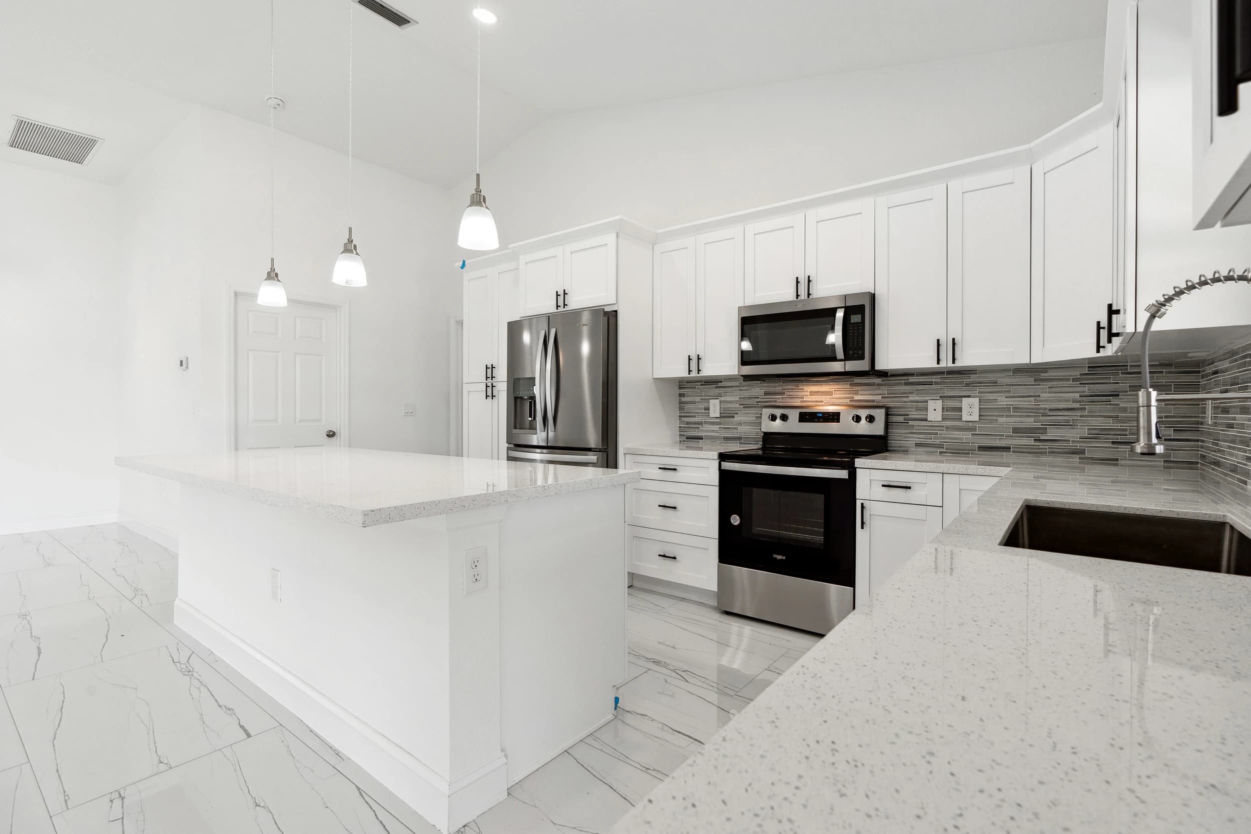 Modern kitchen renovation by Vreeland Roofing in Florida. Elegant white shaker cabinets, quartz countertops, stainless steel appliances, and stylish pendant lighting. Expert home remodeling with high-quality finishes and functional design.