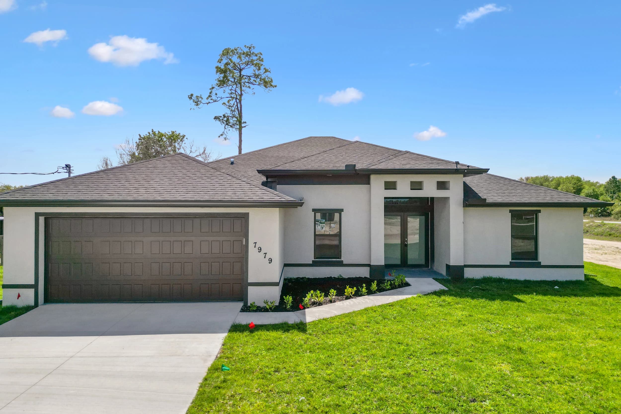 New custom home construction in Florida by Vreeland Roofing. Modern residential property with a sleek black shingle roof, white exterior, and landscaped front yard. Expert home building with durable materials and energy-efficient design.